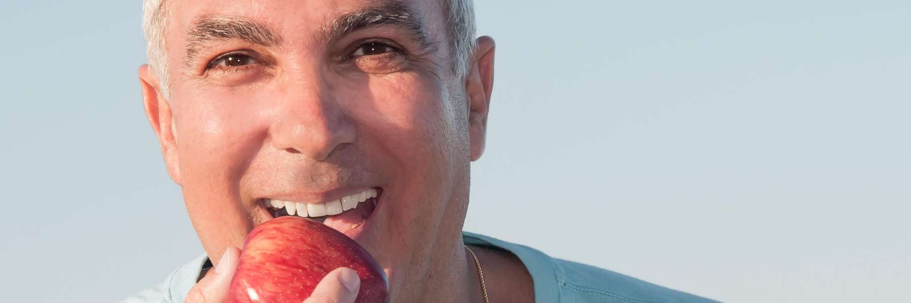 A man with his mouth open is eating an apple, showcasing his dental health in Hermitage