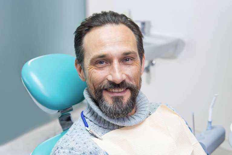 A smiling man sitting in a dentist chair, ready for a dental crown procedure.