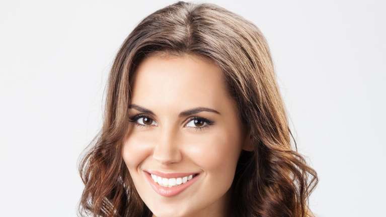 A smiling woman with long brown hair showcases her dental crowns in a warm Hermitage setting