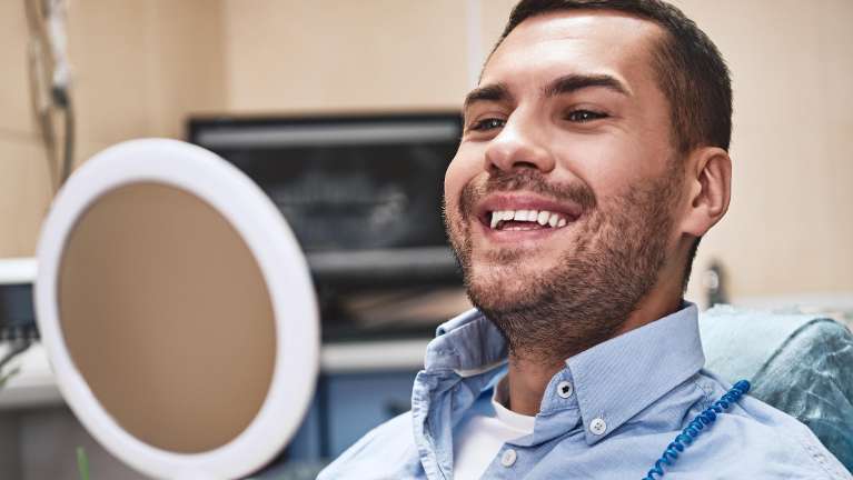 Man looking at himself in the mirror after getting dental crowns in Hermitage, PA